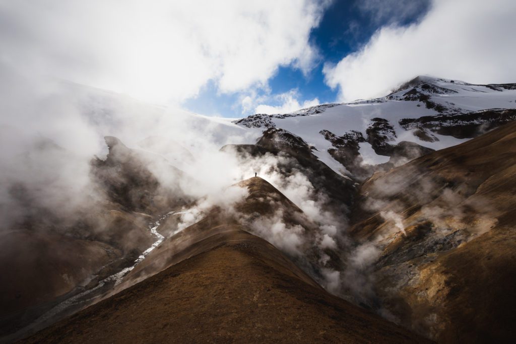 Steaming Hveradalir valley in Kerlingarfjöll with a lone figure on a ridge for scale.