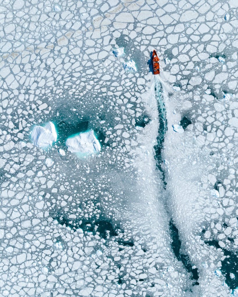 A boat steering through ice near the Eqi glacier in Greenland