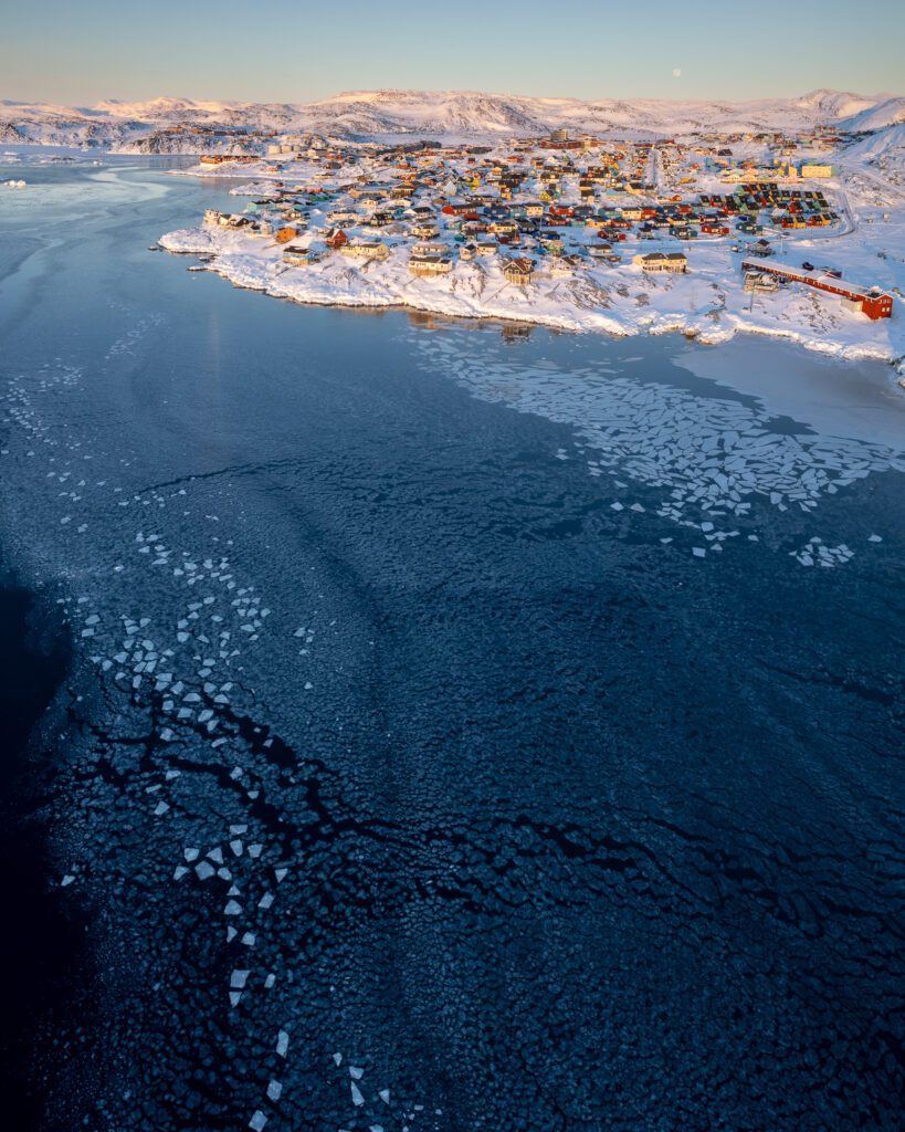 Aerial of Ilulissat town in low winter sun above pancake-ice patterns in Disko Bay, Greenland.