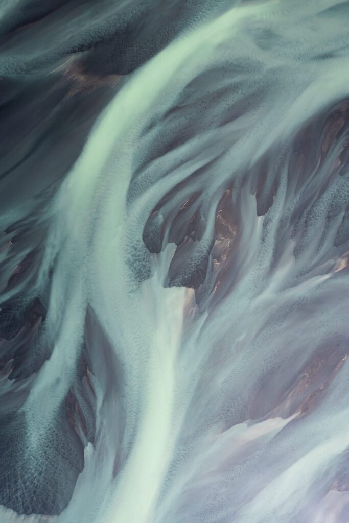 Abstract aerial of pale braided silt rivers flowing over dark Icelandic sand.
