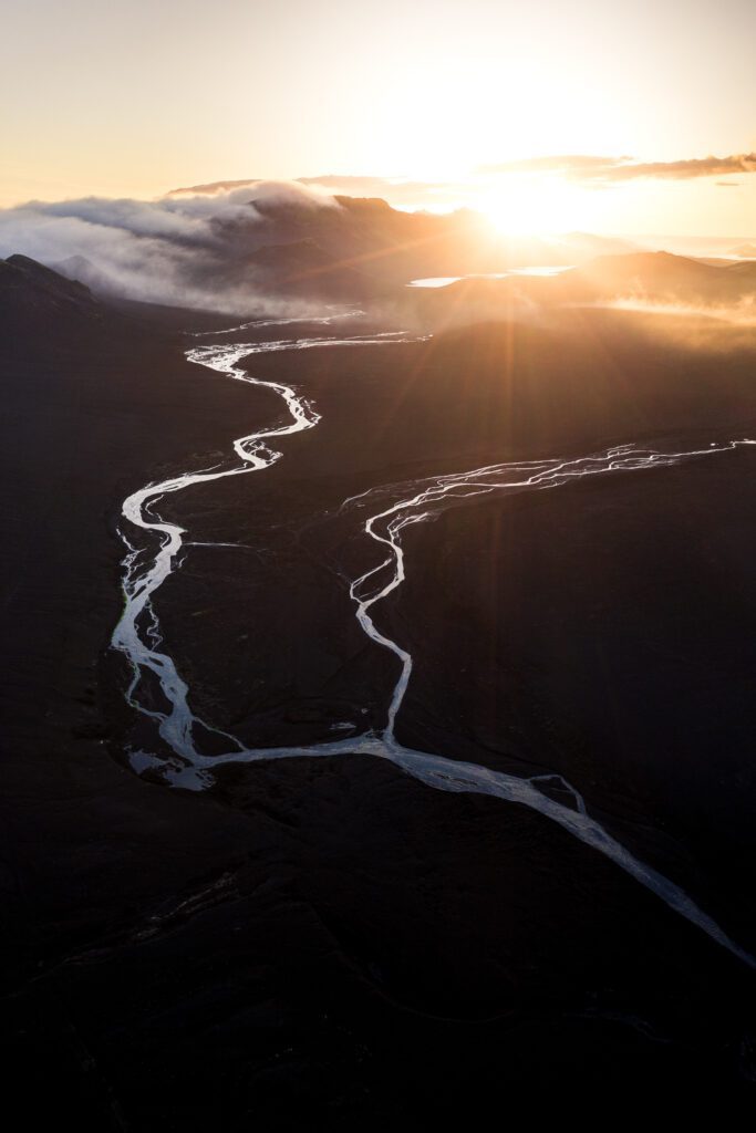Aerial of braided rivers winding through dark Highland valleys at sunrise, Iceland.