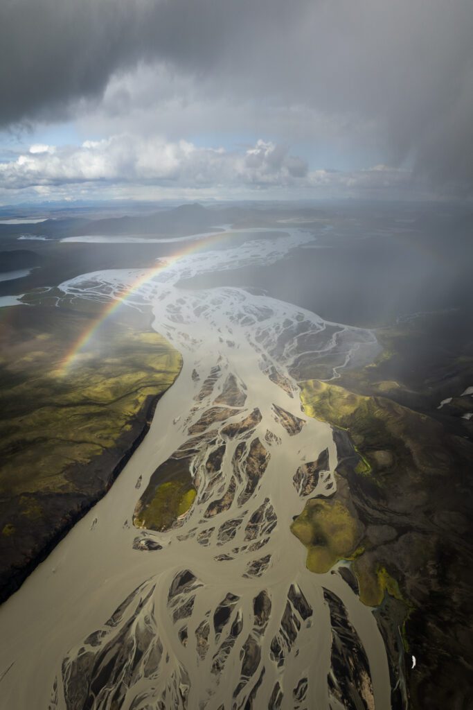 Aerial drone view of a rainbow arching over the braided silt channels of the Tungnaá river, Iceland.