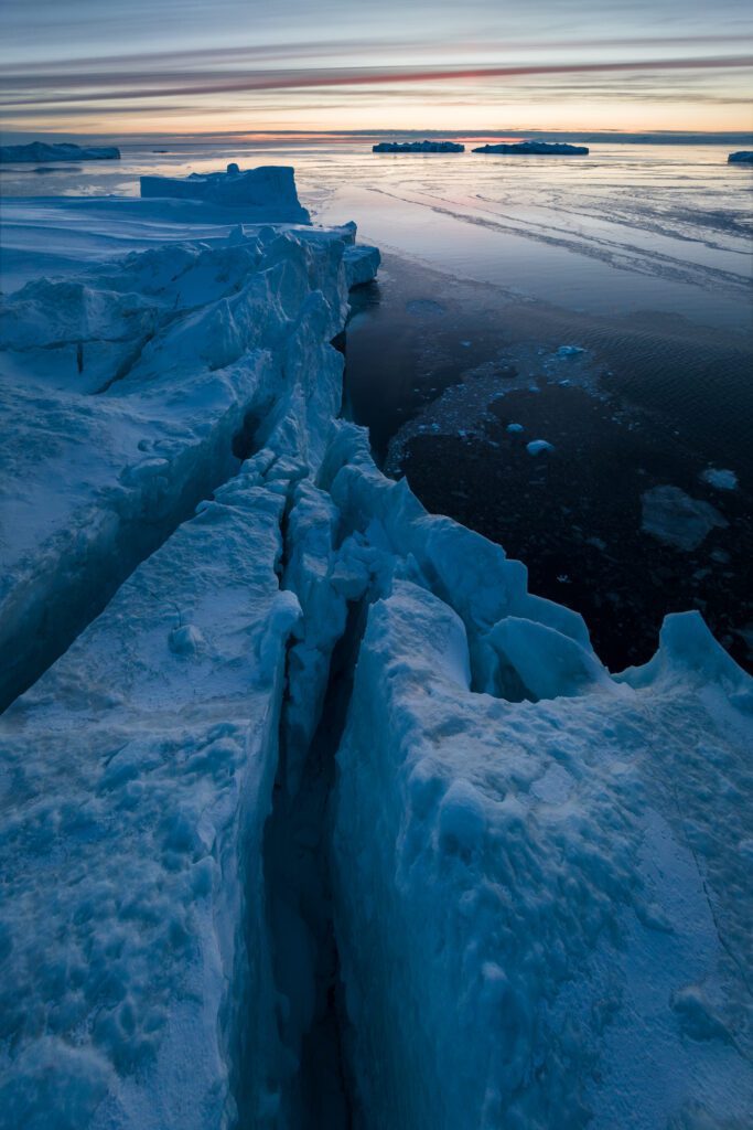 Cracked iceberg surface running toward distant ice floes at dusk in Greenland.