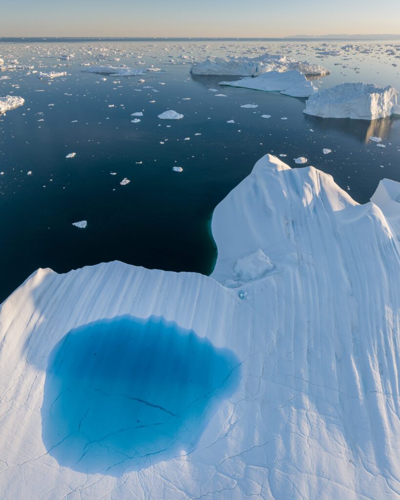 Aerial of a flat iceberg with a deep blue melt pool in front of Disko Bay, Greenland.