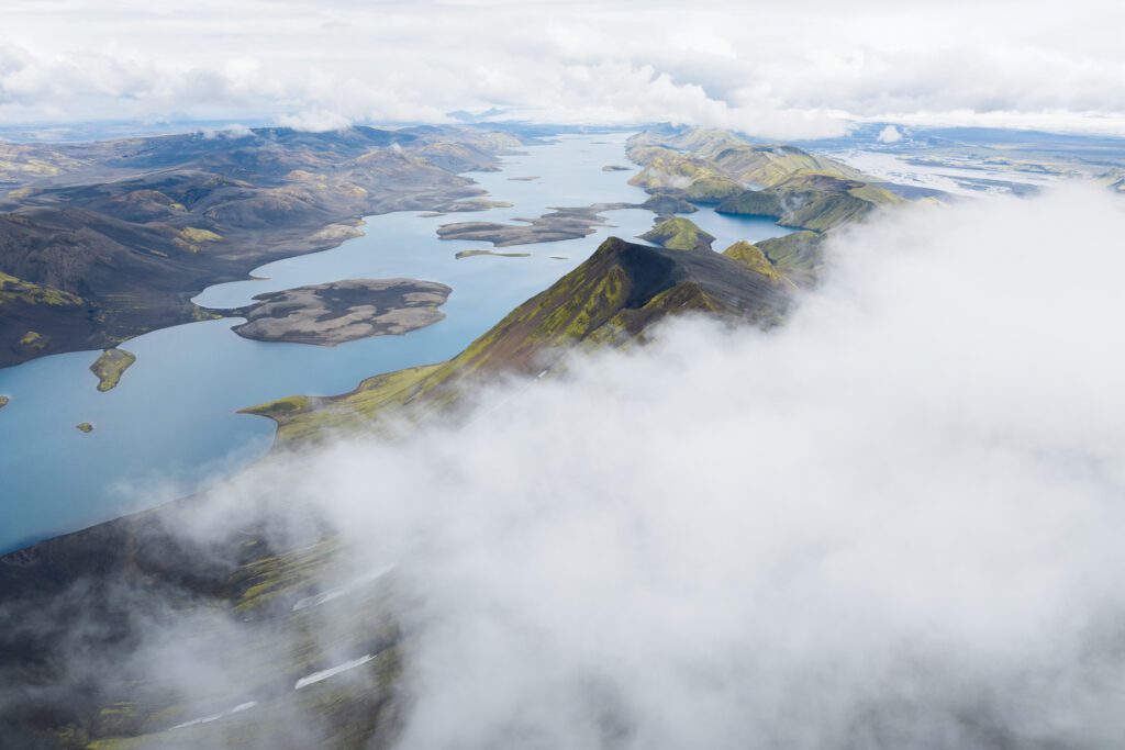 Aerial of a finger-lake system winding through green Highland ridges under low cloud, Iceland.