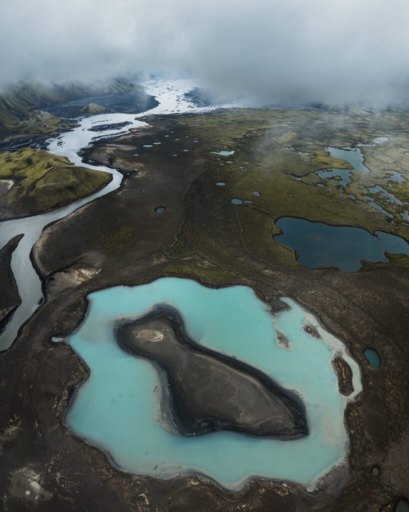 Aerial of a glacier tongue ending in turquoise meltwater pools across a wide dark plain, Iceland.