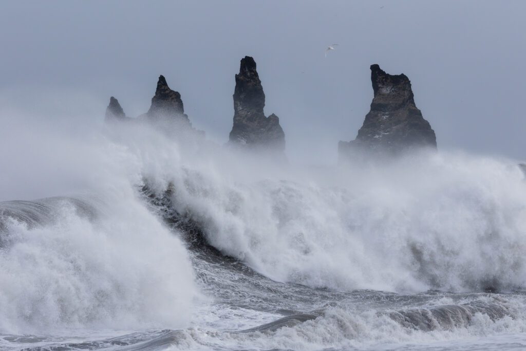 Heavy waves breaking in front of the Reynisdrangar sea stacks under storm-grey skies.