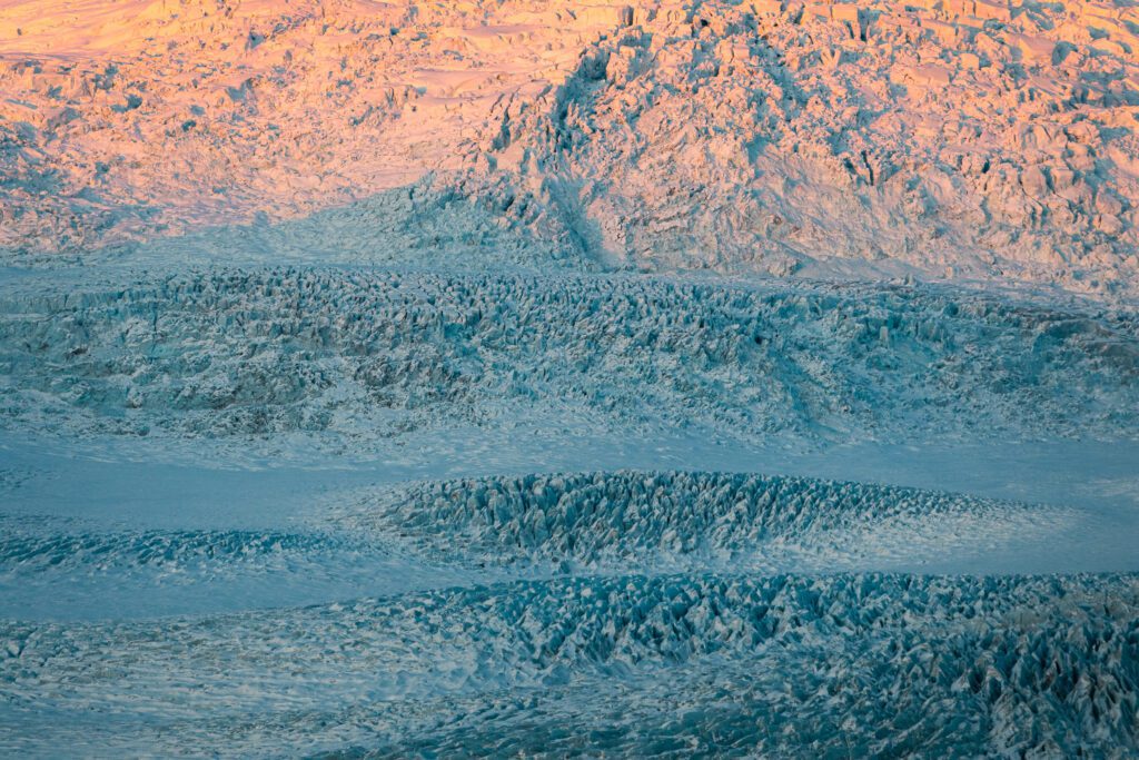 Close-up of crevassed glacier ice at Fjallsárlón glowing pink in alpenglow, deep blue cracks running through.