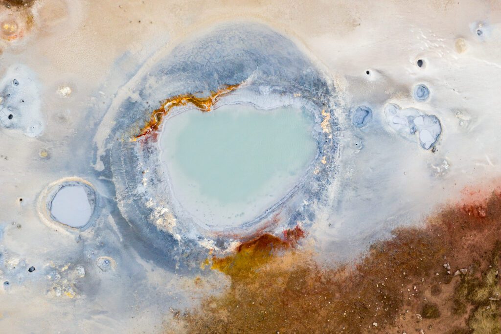 Top-down aerial of a milky turquoise hot pool at Gunnuhver ringed by orange and white mineral crusts.