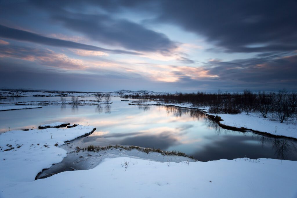Þingvellir in winter, a still river curving through snow with pastel sunset cloud above.