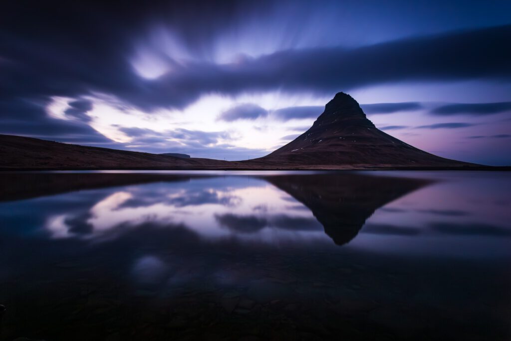 Kirkjufell at blue hour reflected in glass-still water under streaking long-exposure cloud.