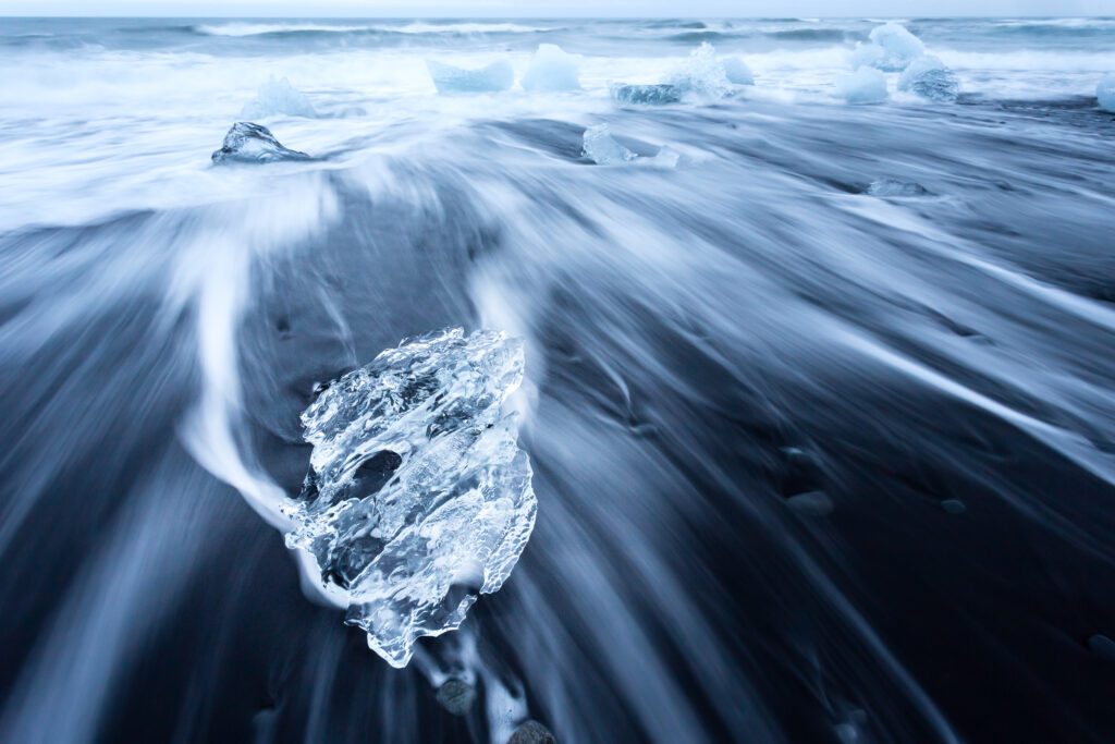 Single piece of clear glacier ice on Diamond Beach, wave wash streaking past it.