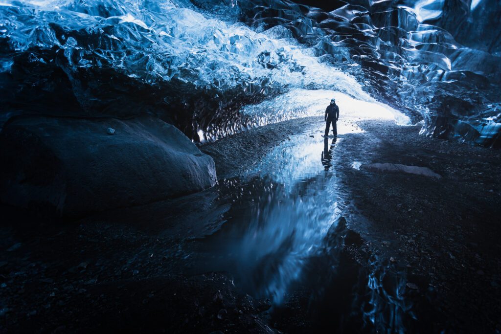 Figure standing inside a blue Vatnajökull ice cave, daylight pouring through the entrance.