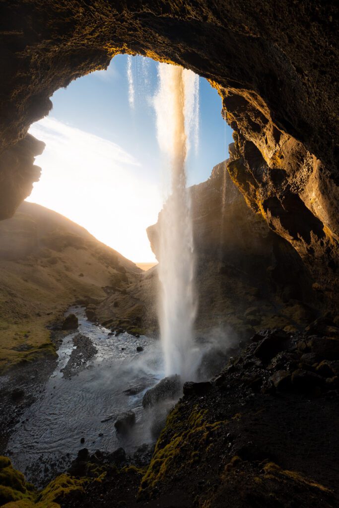 Kvernufoss seen from inside the cave behind it, sun bursting through the falling water.