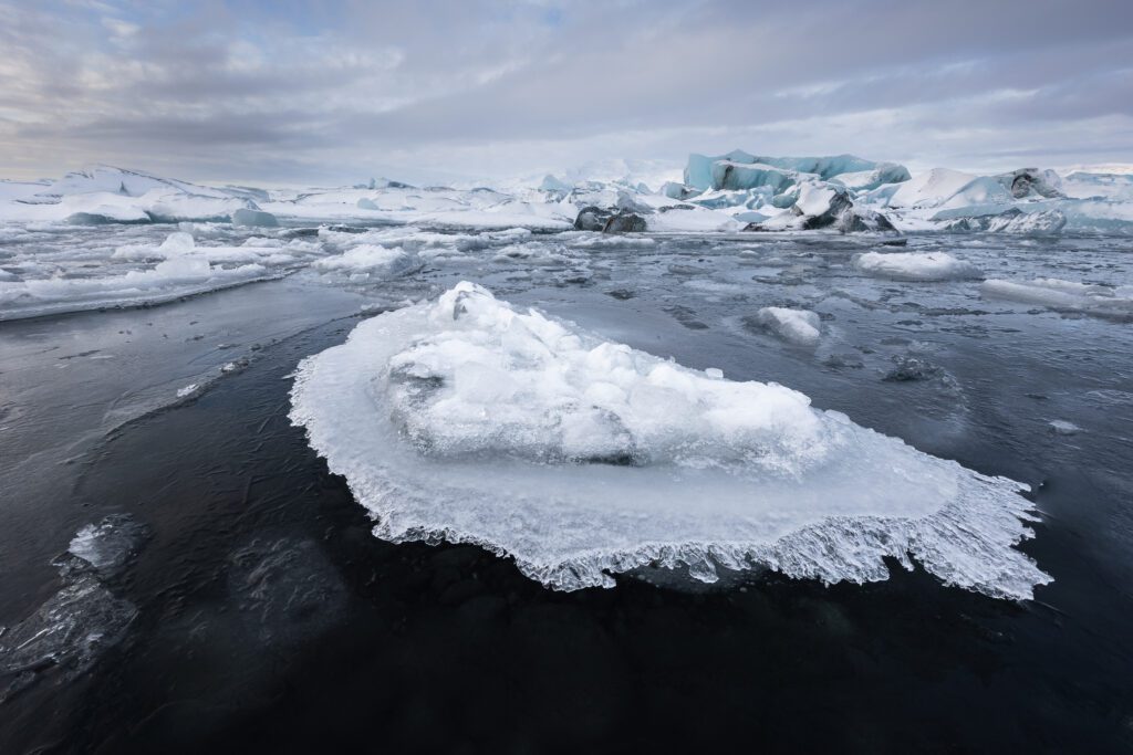 Stranded iceberg sitting on the frozen black surface of Jökulsárlón lagoon at dawn.