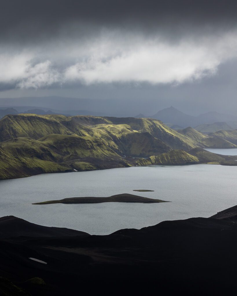 Finger-shaped lake ringed by mossy ridges with two small black islands floating in it.