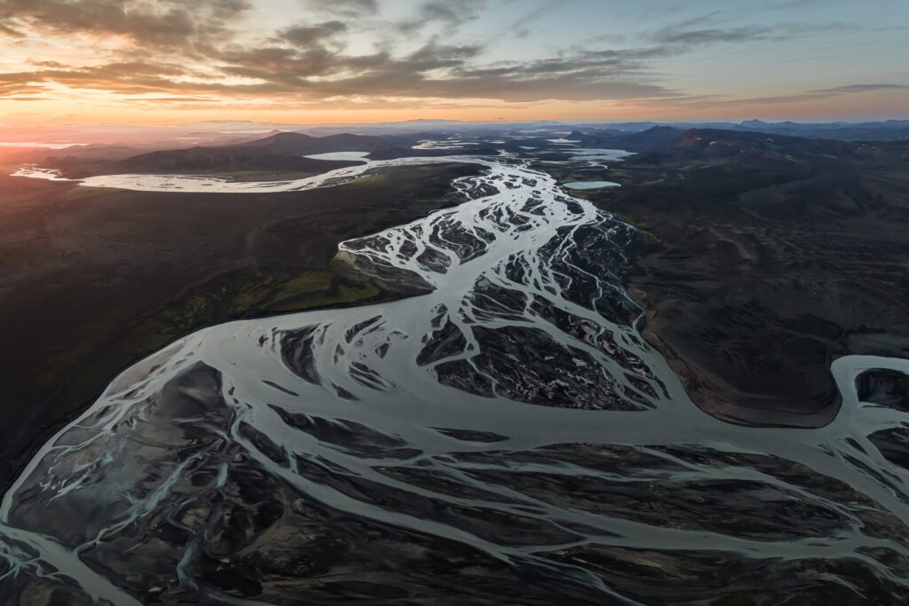 Silver braided rivers fanning across dark sand at sunset, seen from above.