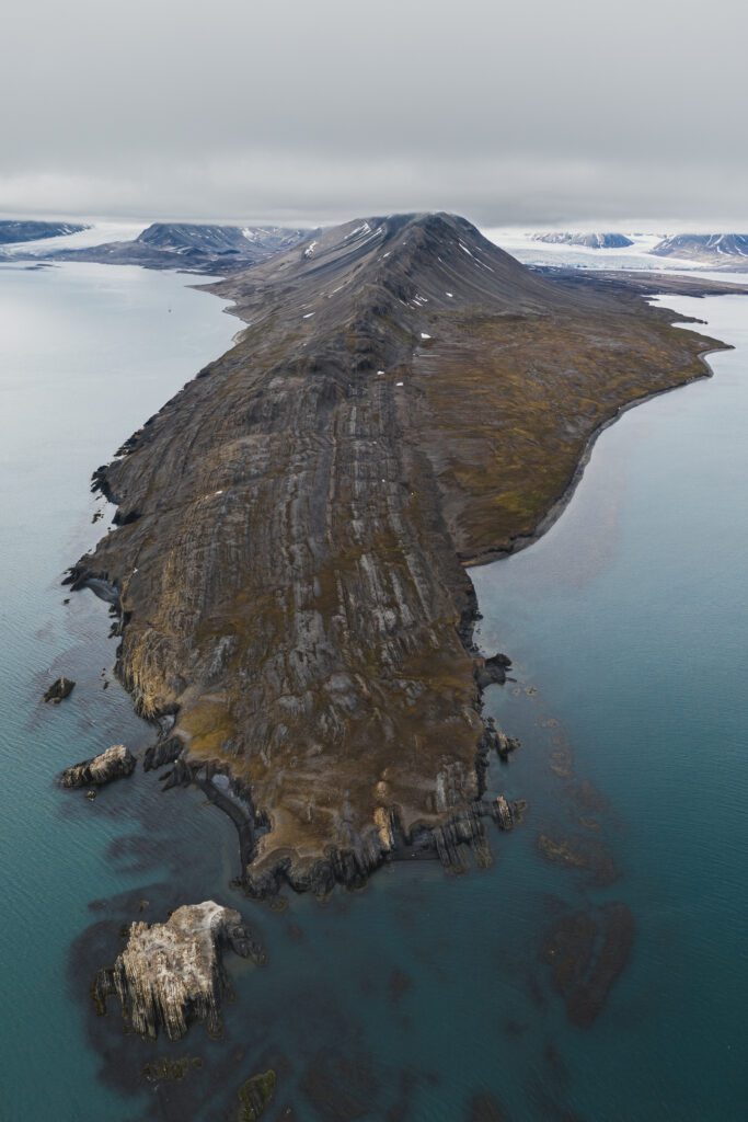Aerial view of a long brown peninsula jutting into turquoise Svalbard waters.