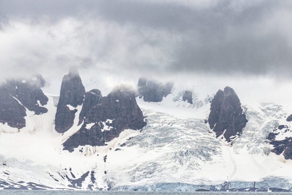Jagged dark peaks and hanging glaciers under blowing snow, Svalbard.