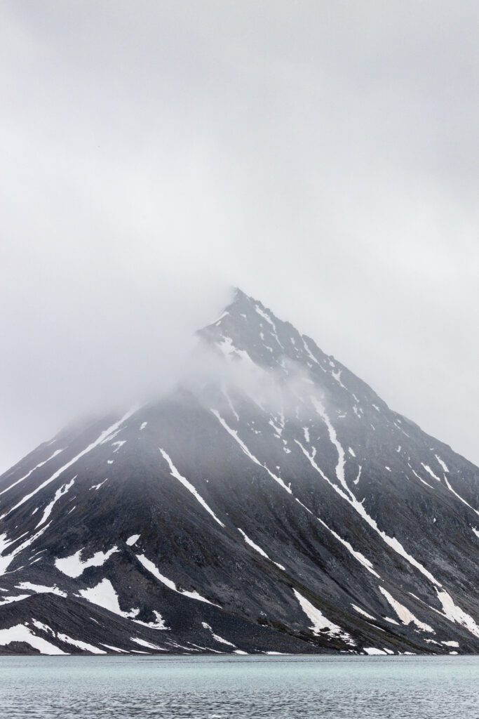 Pyramidal Svalbard peak rising from a calm fjord, summit veiled in mist.