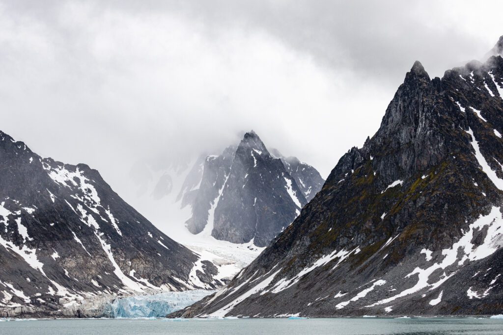 Glacier flowing between jagged peaks into a Svalbard fjord.