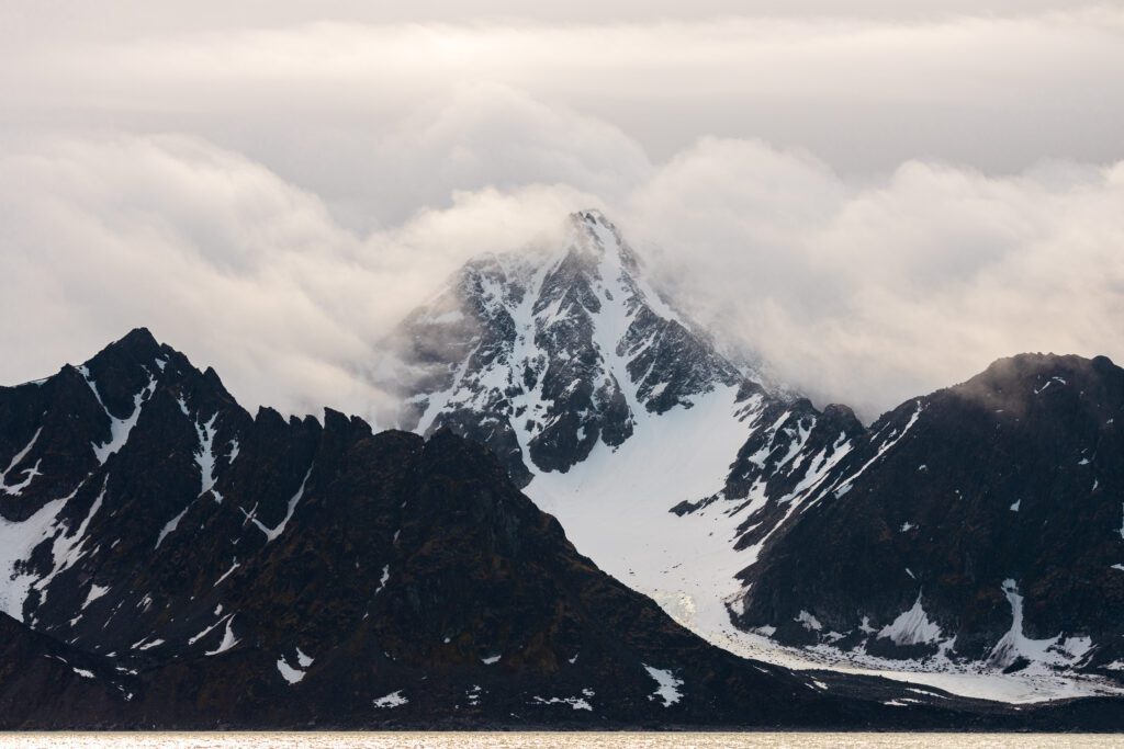 Pyramidal Svalbard peak emerging from clouds above a glacier between dark ridges.