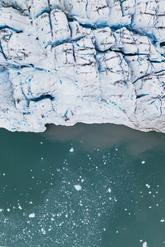 Top-down aerial of a Svalbard glacier front meeting calm water with scattered brash ice.