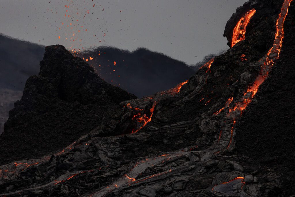 Lava streaming down a smoking cinder cone through dark cooled basalt.