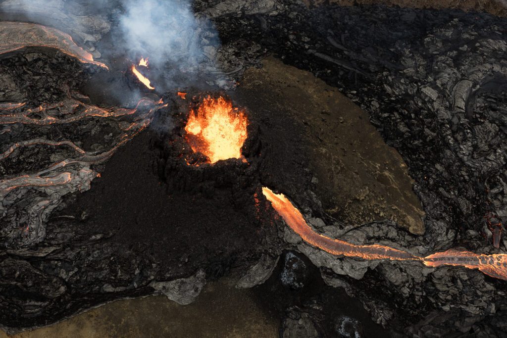 Top-down aerial of a glowing crater vent with lava channels radiating outward.