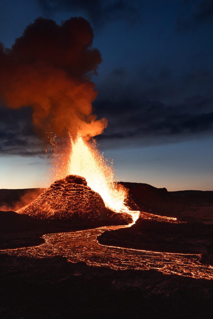 Classic cinder cone eruption with a lava fountain and smoke plume at twilight.
