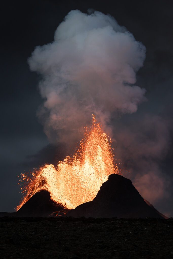 Twin-peaked spatter cone with a massive lava fountain at night.