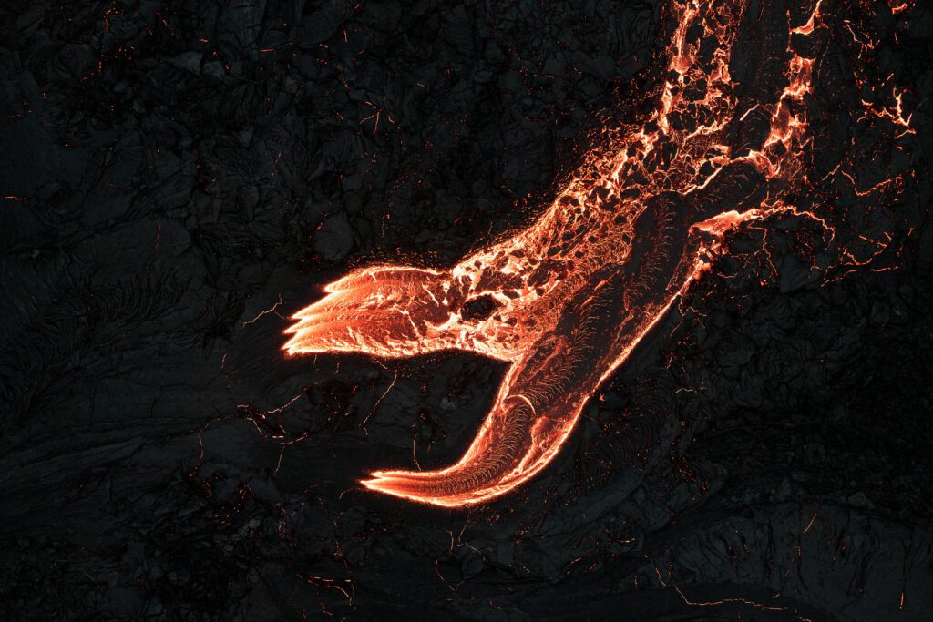 Aerial top-down of a dragon-shaped lava flow advancing across dark basalt.