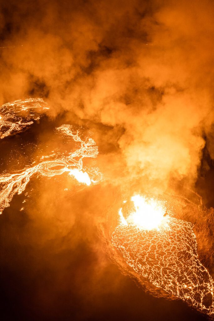 Multiple lava vents and channels glowing through dense smoke at night.