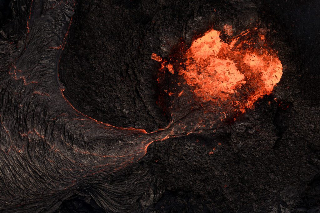 Top-down close-up of a lava vent breakout flowing across rope-textured basalt.
