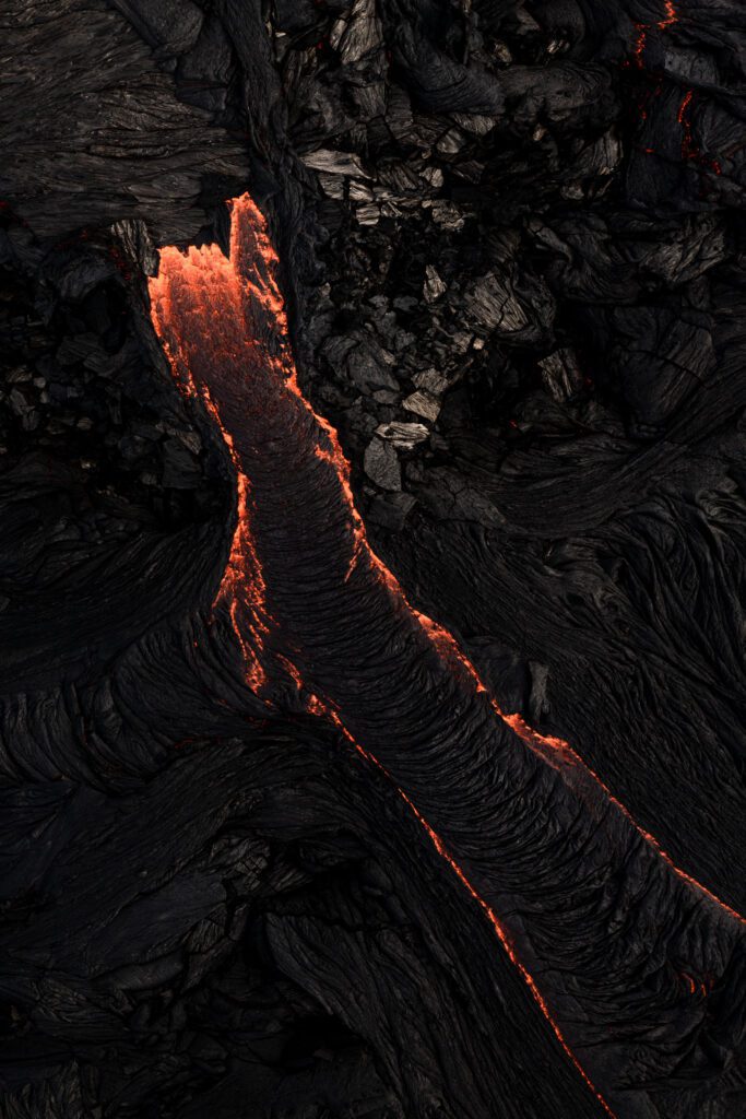 Small lava breakout flowing through cooled black basalt, abstract close-up.