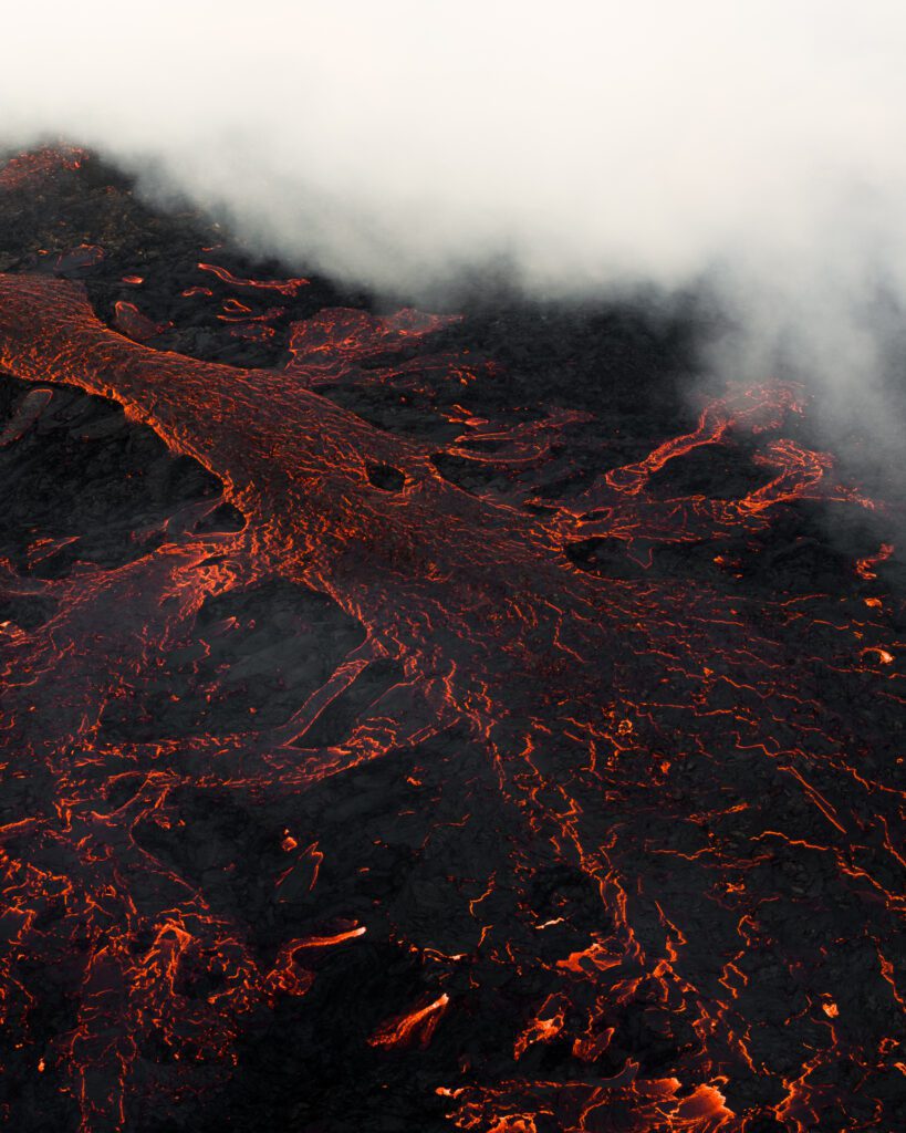 Aerial of a fresh lava field with glowing cracks beneath low cloud.
