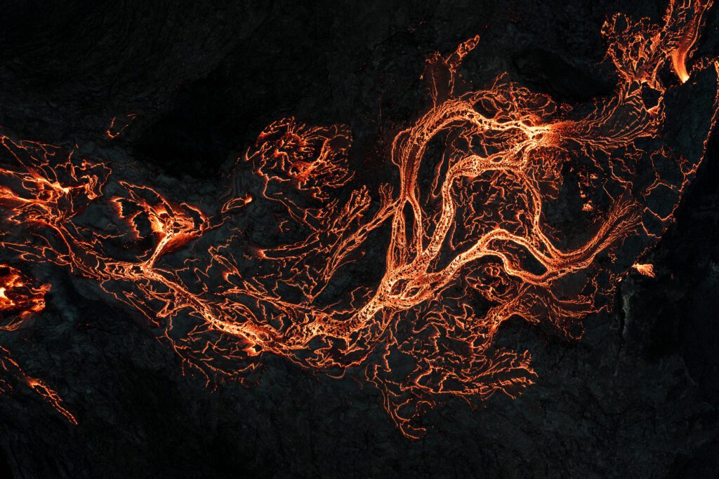 Top-down aerial of braided glowing lava channels across dark basalt.