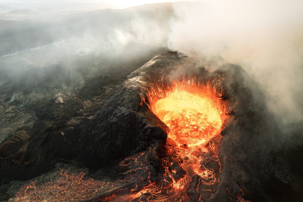 Aerial of an erupting crater with a bubbling lava lake and drifting steam.