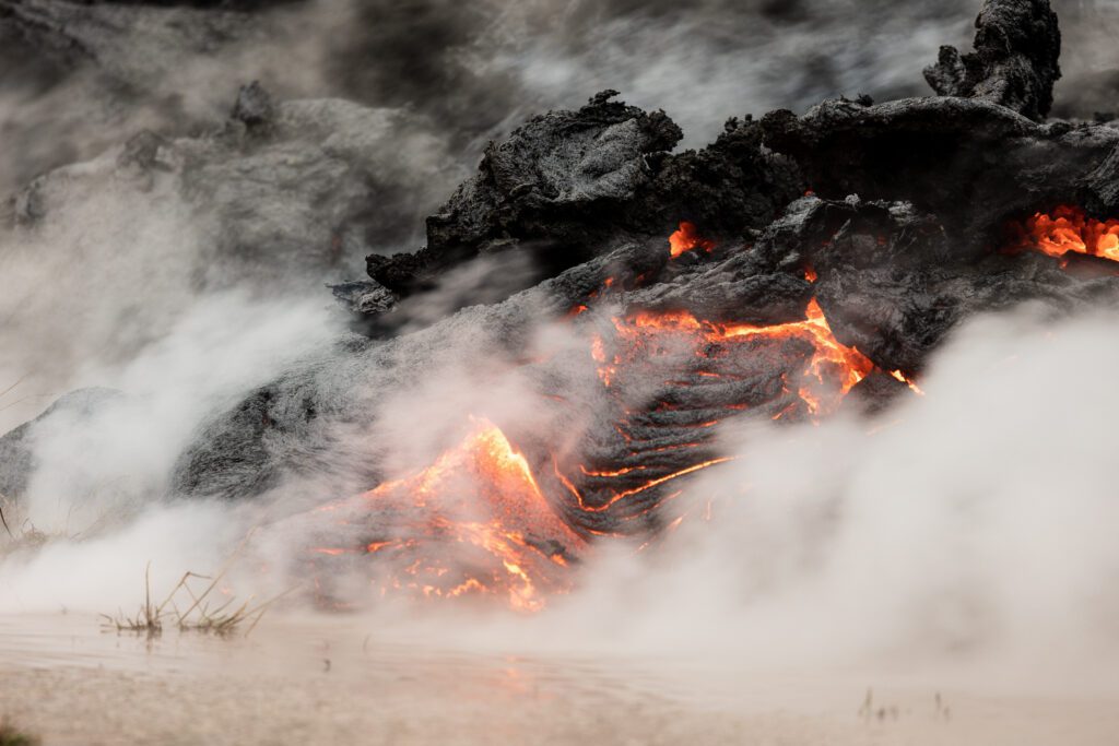 Lava flow front meeting wet ground with thick steam rising.