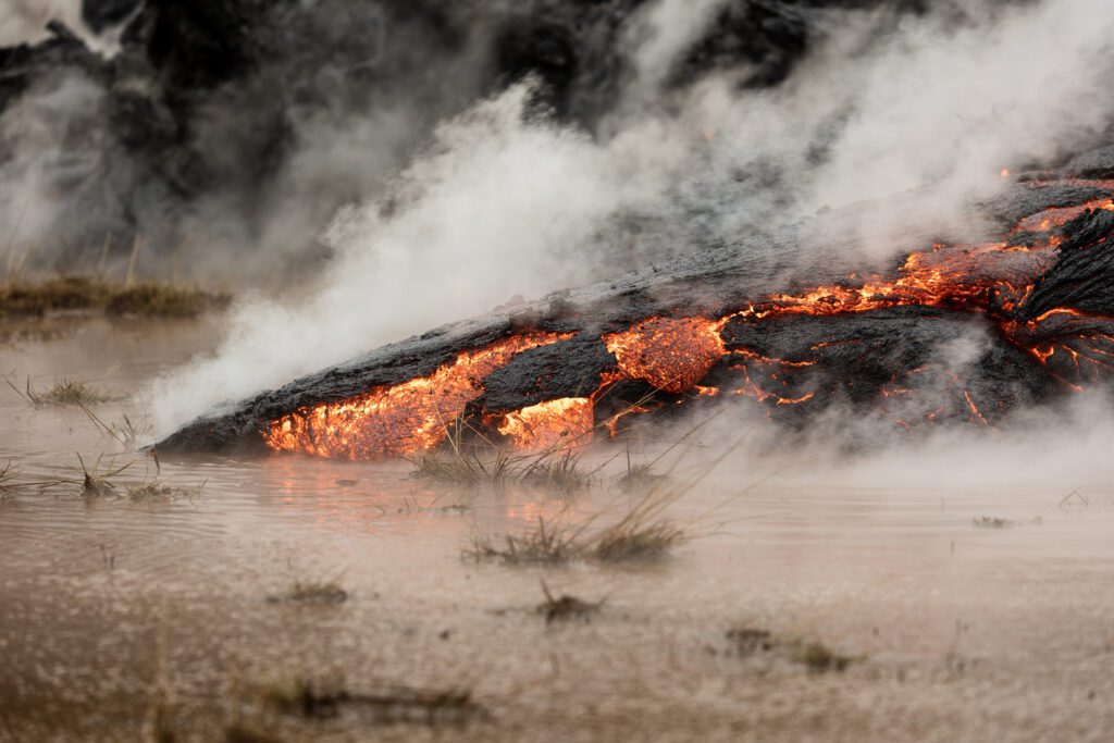 Glowing lava flow meeting boggy ground and steam during an Iceland fissure eruption.