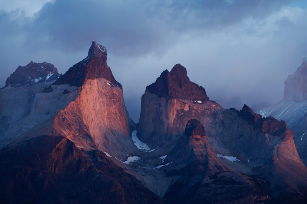 Dawn light catching the granite faces of Los Cuernos del Paine through cloud.