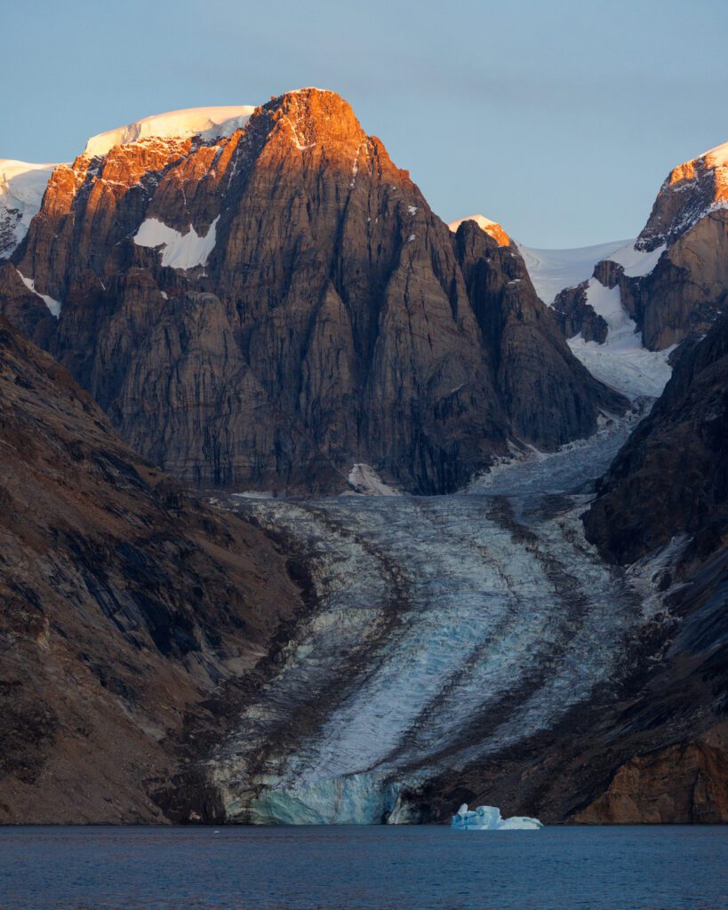 Sunrise alpenglow on a basalt peak above a hanging glacier in Scoresbysund, East Greenland.