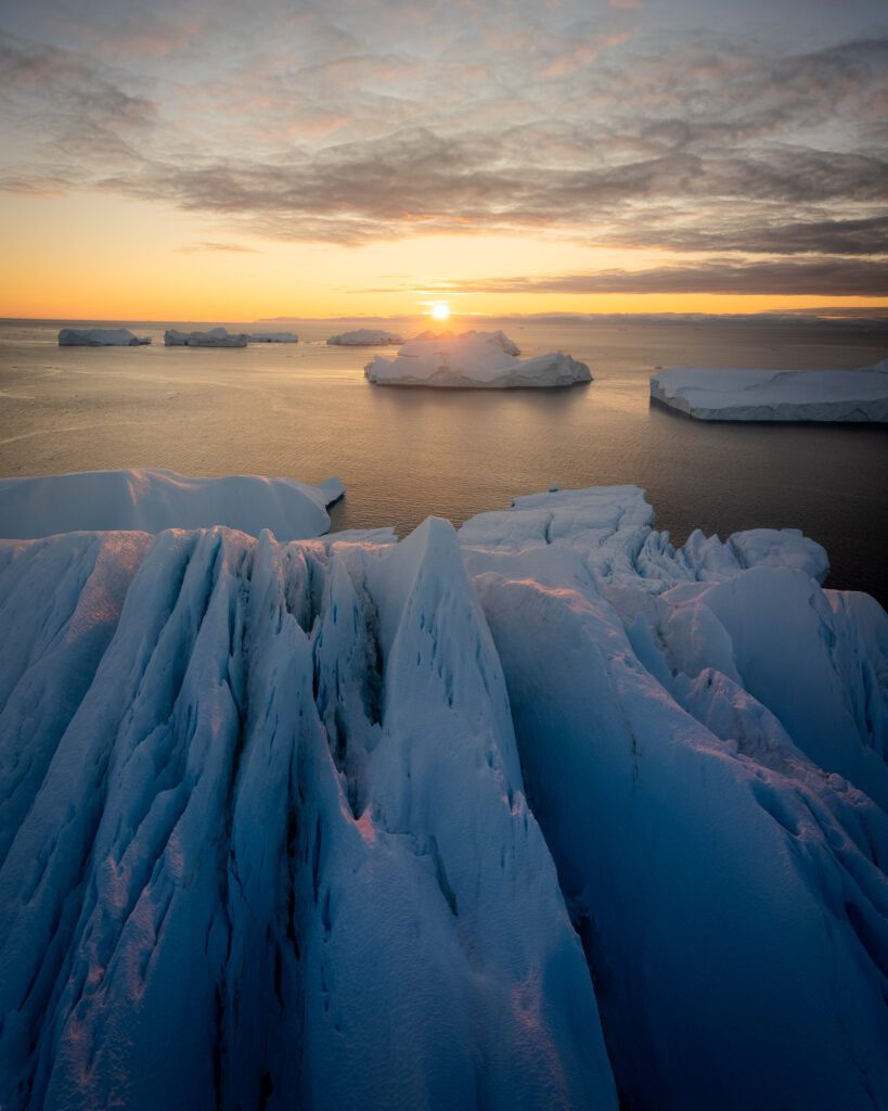 Sunrise over jagged blue iceberg ridges in Disko Bay, Greenland.