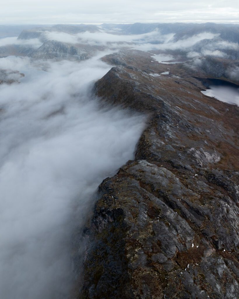 Aerial drone view of a misty cloud-cloaked ridge above a Greenland fjord.