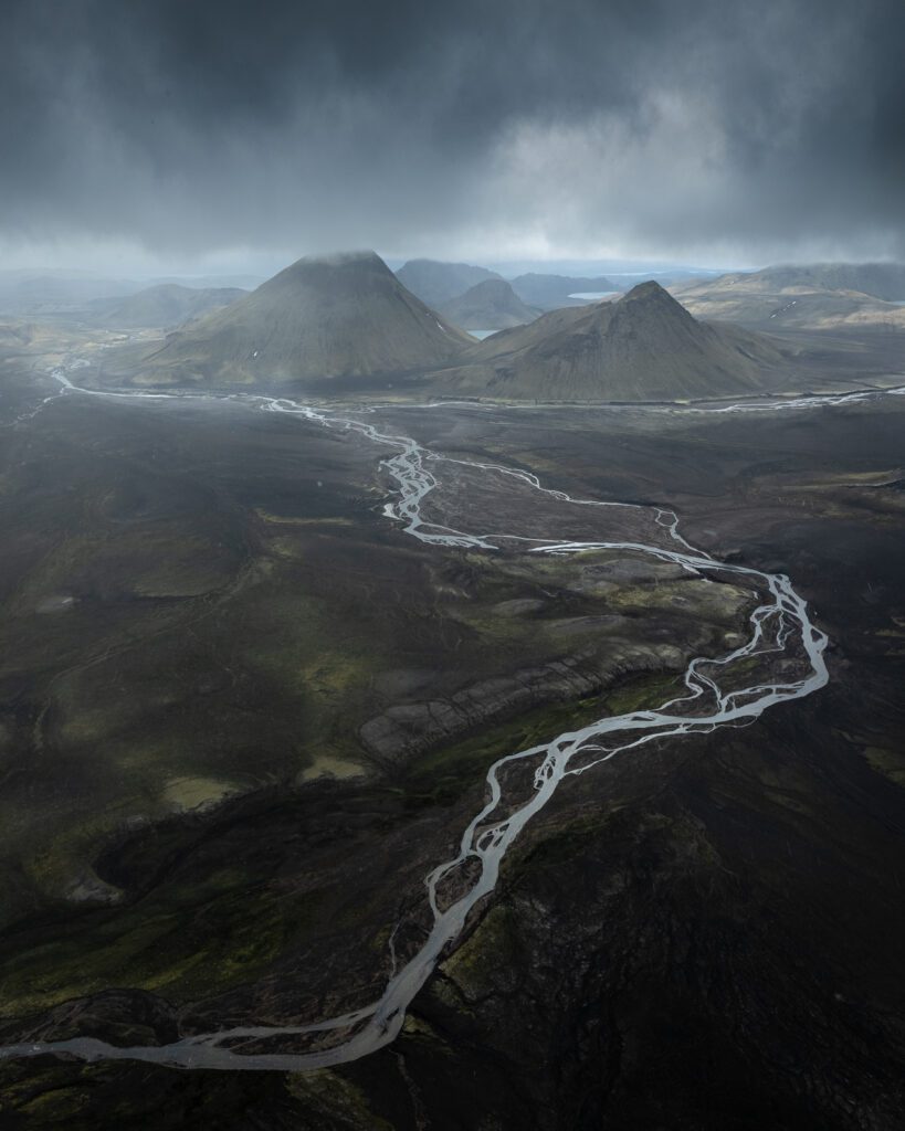 Small glacier tongue ending in braided meltwater rivers across a wide dark plain, seen from above.