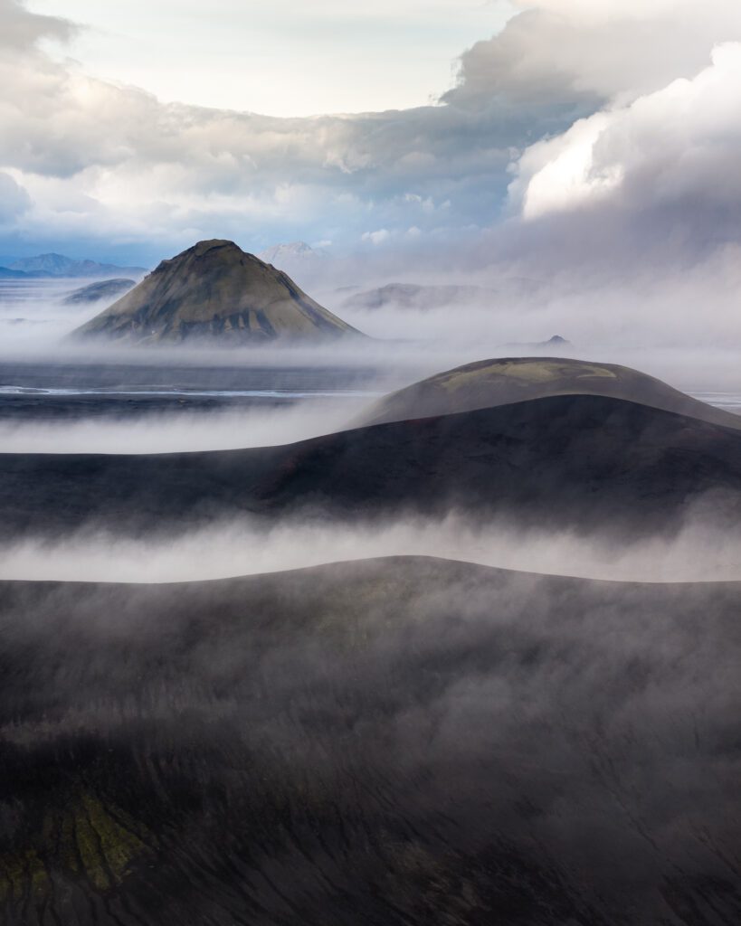 Green ridges descending into a vast finger-lake system under low drifting cloud, seen from a drone.