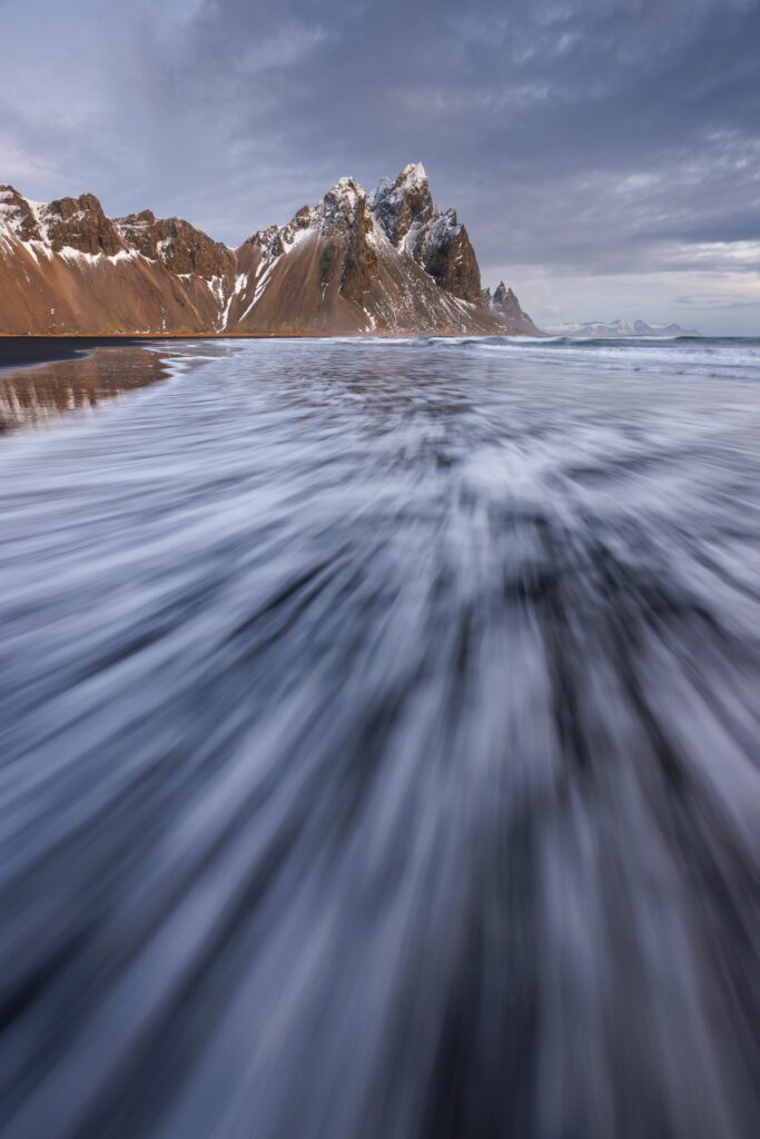 Vestrahorn at Stokksnes with shallow wave wash streaking across the black sand toward the camera.