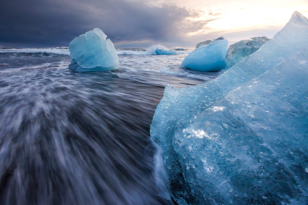 Diamond Beach: chunks of clear iceberg ice resting on black sand as a wave rushes in.