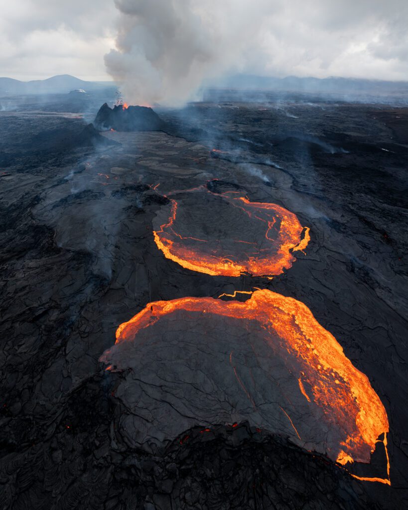 Aerial of the Fagradalsfjall eruption with two glowing lava pools and a smoking cone.