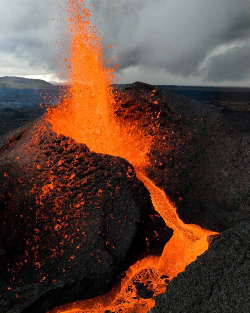 Aerial drone shot of an erupting cinder cone with a fountain and lava river snaking down.